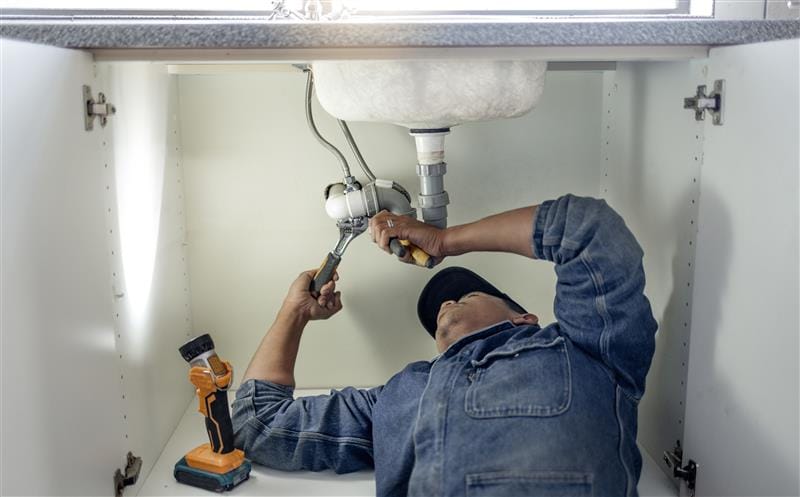 Plumber repairing pipes beneath a bathroom sink in Port Hueneme